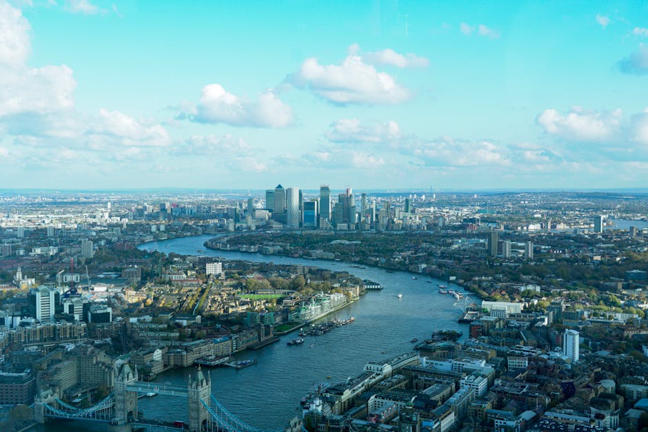 An aerial view of central London showcasing the River Thames winding through the cityscape, with numerous boats docked along the banks and modern high-rise buildings clustered in the Canary Wharf area